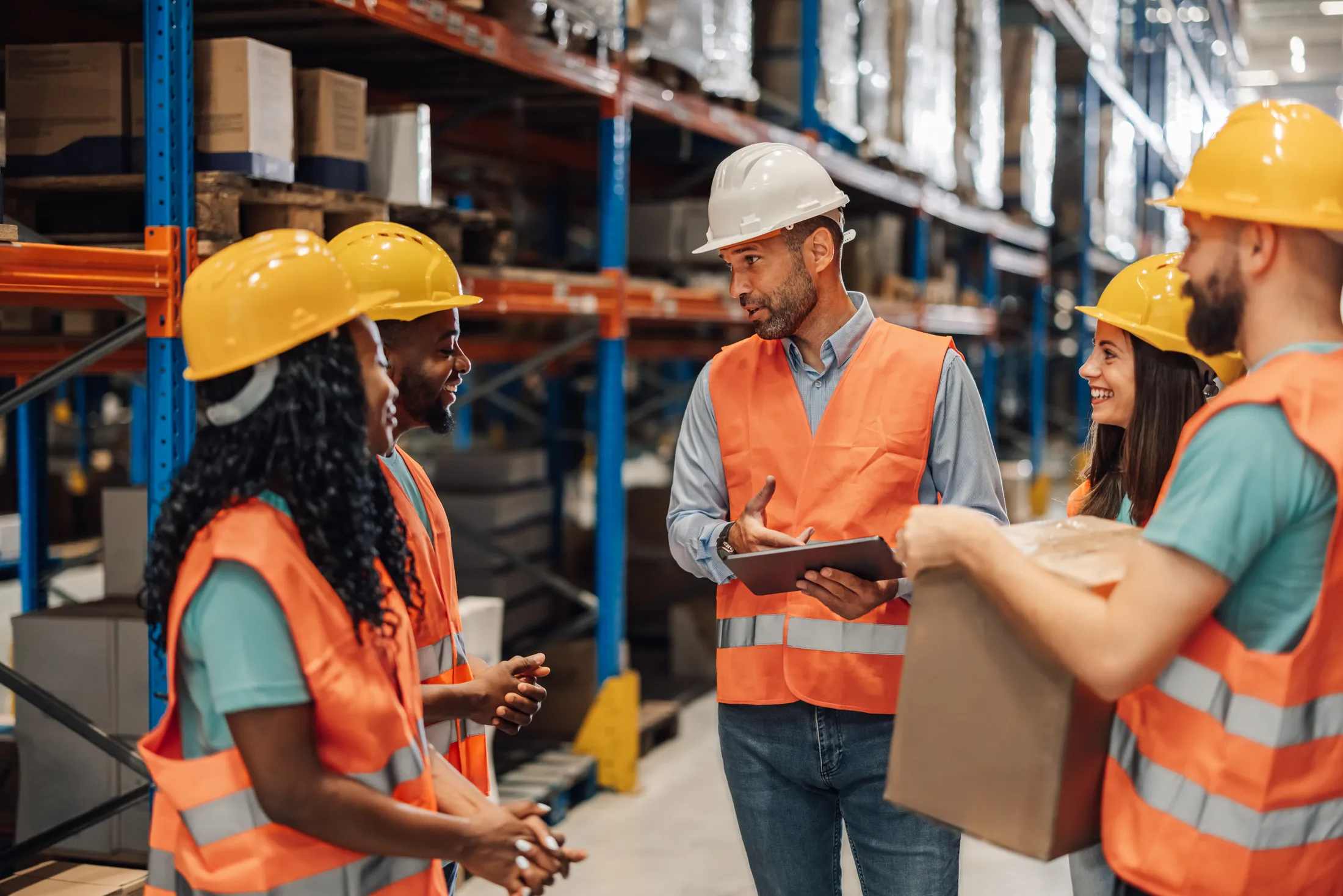 A supervisor with a tablet briefing a warehouse crew in high-visibility vests