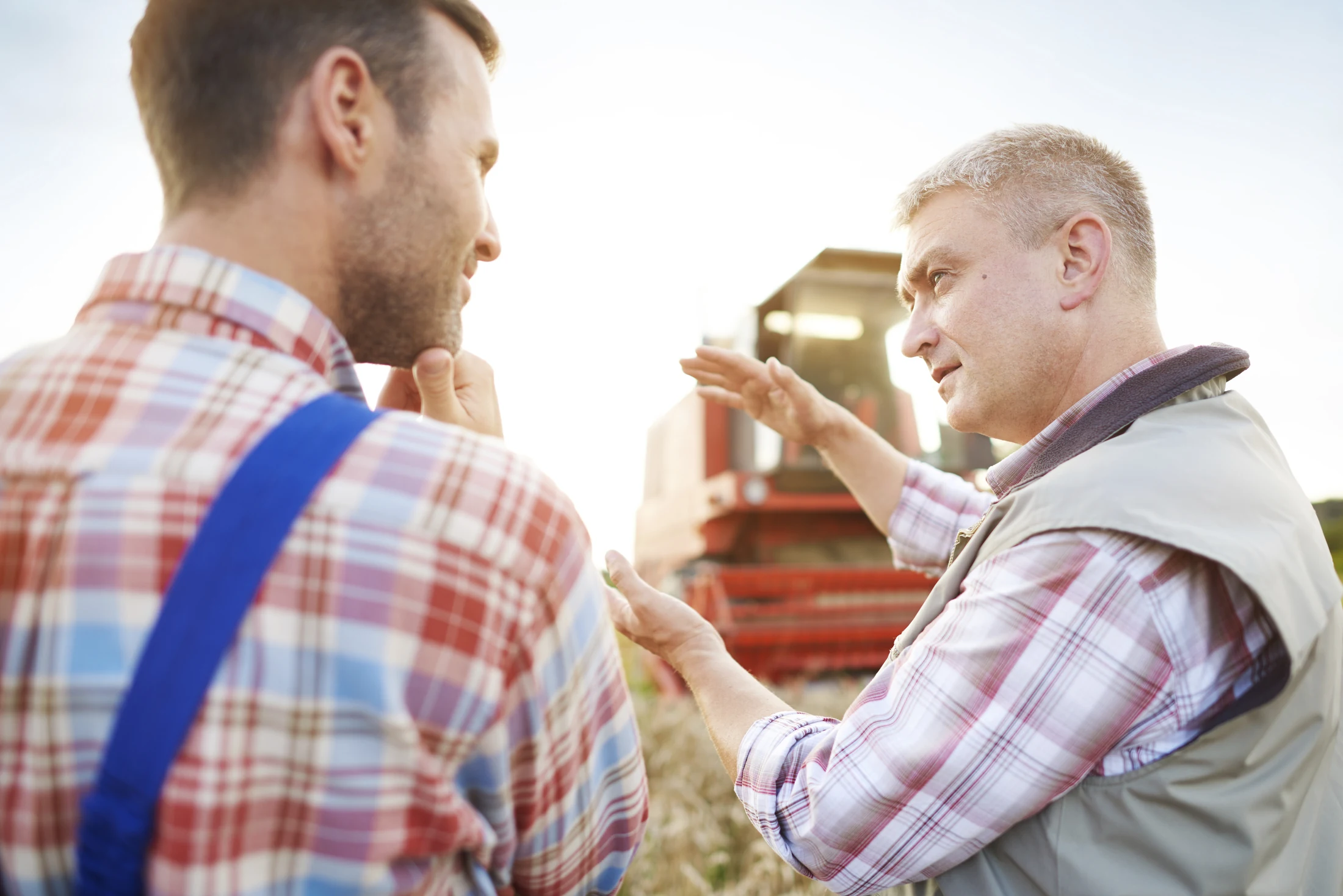 Two farmers talking in a wheat field beside a combine harvester