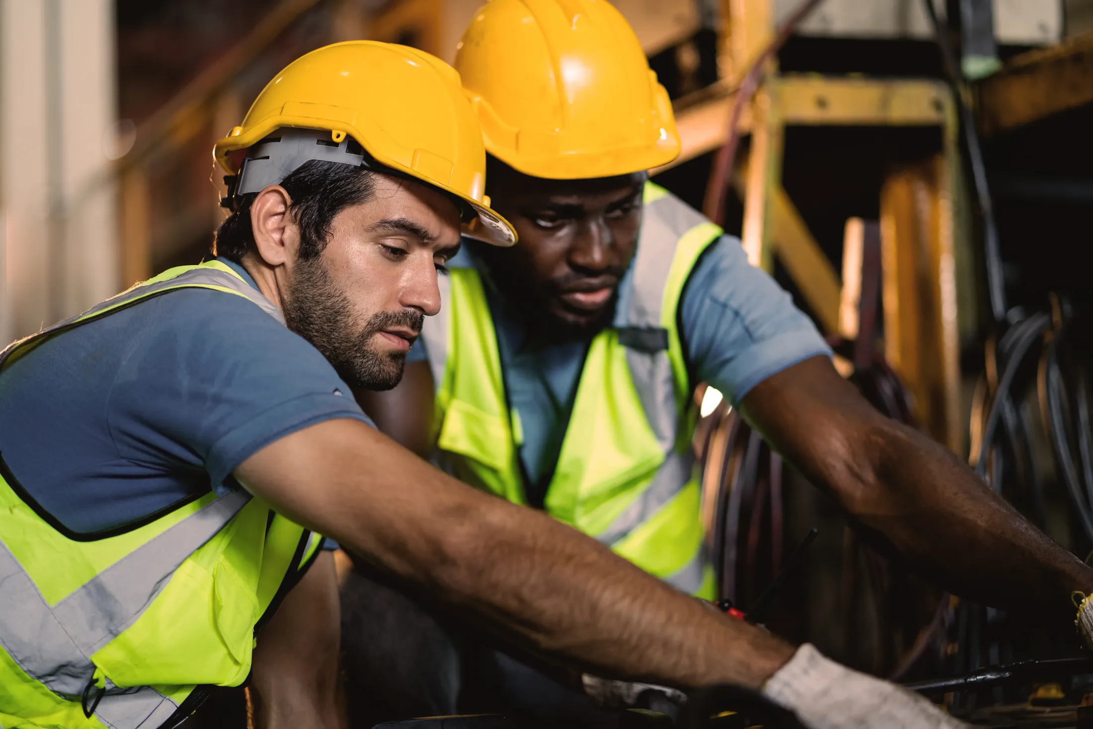 Two workers in hard hats and high-visibility vests working on equipment together